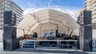 Konligo Fastival event structure with full white inner backdrop and membrane used as a covered outdoor stage setup with musical instruments and speakers, now available on MTN SHOP US.