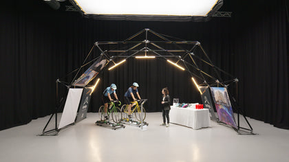 Indoor setup of Konligo event structure featuring two cyclists on stationary bikes and a display table with helmets and water bottles. Now available on MTN Shop US.
