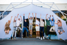 Group of people jumping in front of a Konligo Fastival event structure with a white membrane cover, celebrating outside a modern industrial building, now available on MTN Shop US.